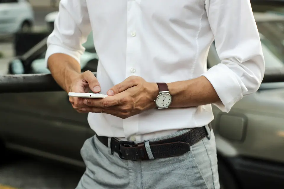 Sales rep checking an order on his phone next to his car